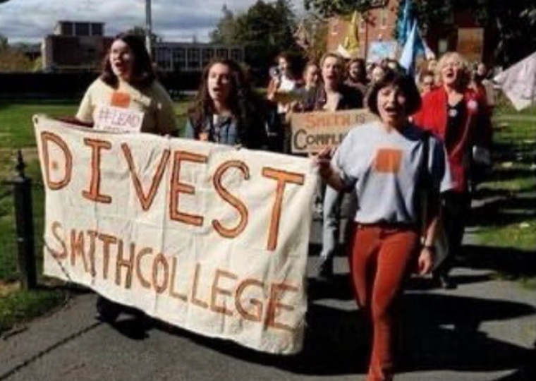A group of students hold up a cloth textured sign that reads "Divest Smith College" in orange letters