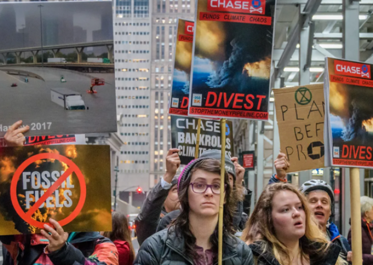 A group of people stand outside wearing jackets and carrying signs that read "Chase Funds Climate Chaos"