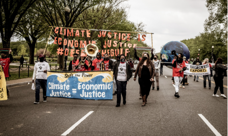 A group of people walking down the street while holding a sign that reads "Climate Justice = Economic Justice"