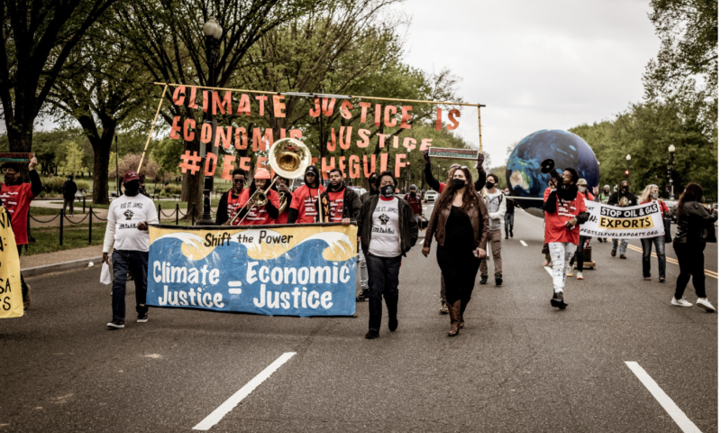 A group of people walking down the street while holding a sign that reads "Climate Justice = Economic Justice"