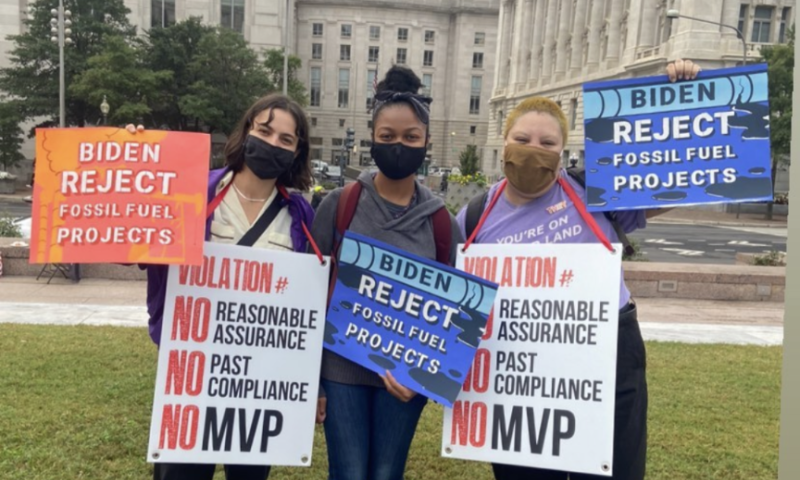 PSN staff are wearing masks and holding signs that read, "Biden reject fossil fuel projects" 
